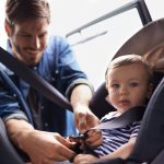 A young father strapping his baby into a car seat.